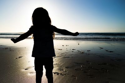 Silhouette girl standing on shore at beach against sky