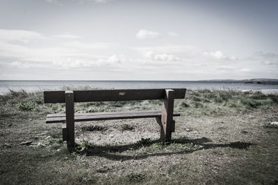 Empty bench on beach against sky