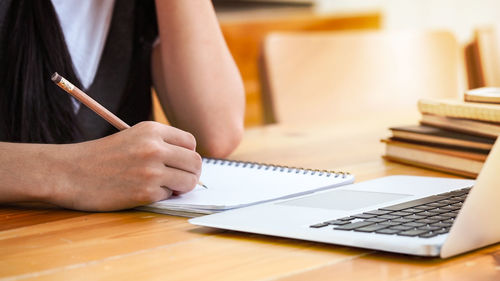 Midsection of woman writing in book at desk