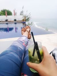 Low section of woman with drink at swimming pool against sky