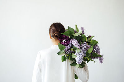 Rear view of woman with bouquet against white wall