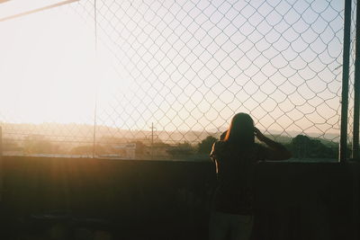 Rear view of woman standing by fence against sky