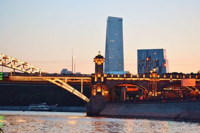 Bridge over river by buildings against sky during sunset