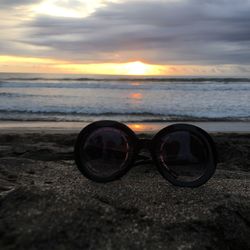 Close-up of sunglasses on beach against sky during sunset