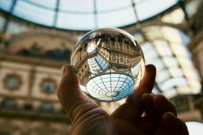 Cropped hand holding crystal ball against glass ceiling of galleria vittorio emanuele in milan