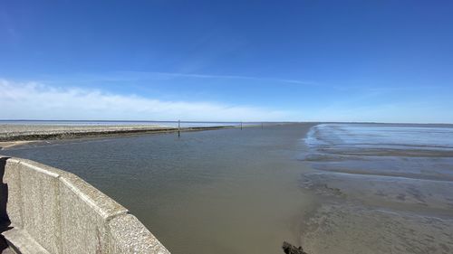 Scenic view of low tide sea against blue sky 