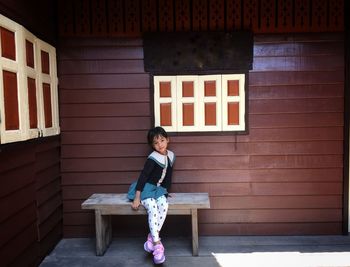 Full length of girl sitting on bench against wall