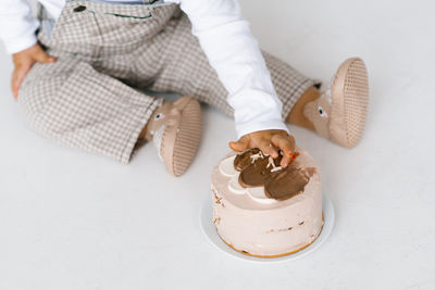 Baby is sitting on the floor and reaching for a cake. the cake is decorated with frosting