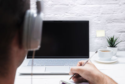 Man on his back with headphones taking notes while looking at the laptop on white background.