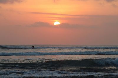 Scenic view of surfer and sea against sky during sunset