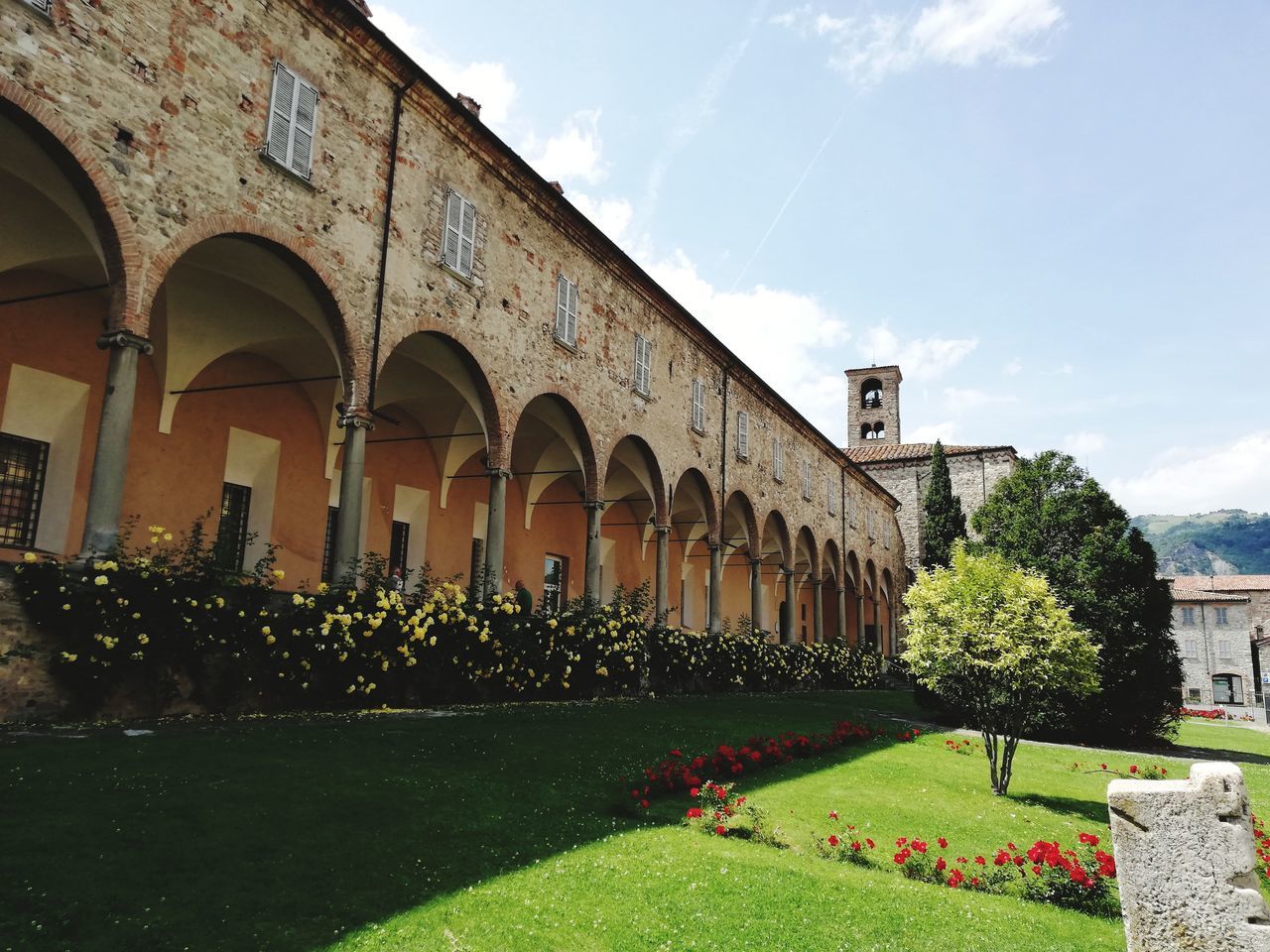 built structure, architecture, plant, arch, building exterior, nature, sky, flower, flowering plant, day, cloud - sky, no people, grass, architectural column, building, growth, tree, outdoors, the past, history, hedge, colonnade, courtyard, arched