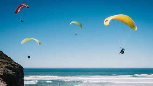 People paragliding at beach against clear blue sky