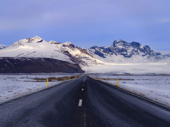 Road amidst snowcapped mountains against sky