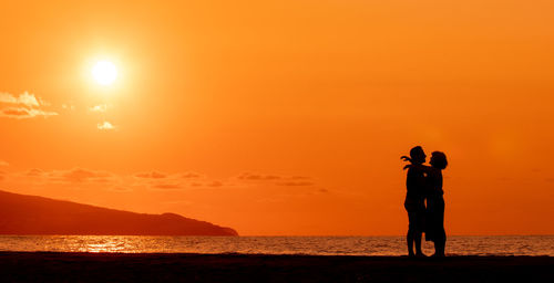 Couple embracing at beach, silhouette in sunset, love and friendship.