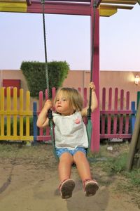 Full length of cute girl sitting on swing in playground