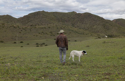 Adult man in cowboy hat and his dog standing on field against sky