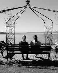 Rear view of couple sitting on shore against clear sky