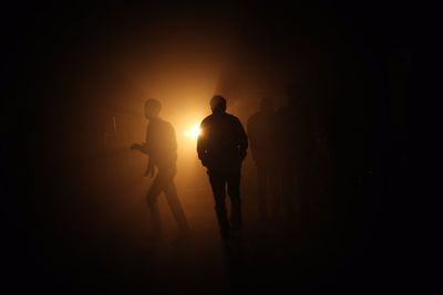 Silhouette men walking on street with car headlight glowing in background