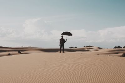 Rear view of man holding umbrella on desert against sky