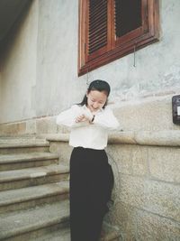 Young woman checking time on wristwatch while standing outside house