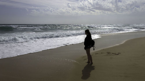 Rear view of woman standing on beach against sky