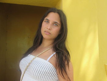 Portrait of young woman standing against yellow wall