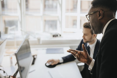 Businessman gesturing and explaining male entrepreneur over desktop pc at office