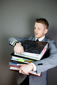 Tired businessman holding stacked files against gray background