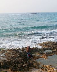 High angle view of man fishing while standing on rock in sea