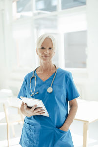 Smiling female doctor holding tablet pc standing with hand in pocket