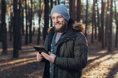 Smiling bearded young man holding digital tablet in forest