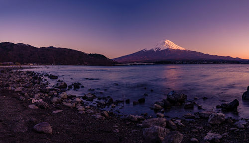 Scenic view of sea by mountains against sky during sunset