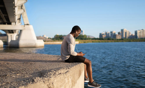 Man sitting by sea against clear sky