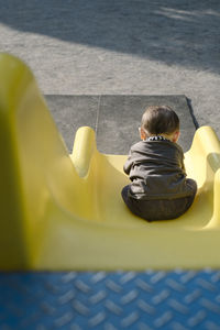 Rear view of baby boy sitting on slide in playground