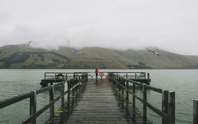 Woman on a red jacket standing at port levy jetty, banks peninsula, nz