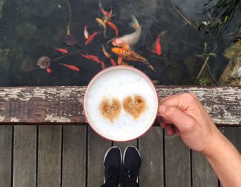 Low section of man holding coffee cup on footbridge over pond