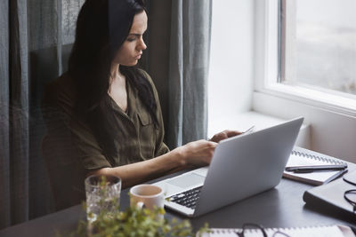 High angle view of woman working at table with laptop seen through glass in office