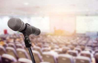 Close-up of microphone with people sitting on chairs