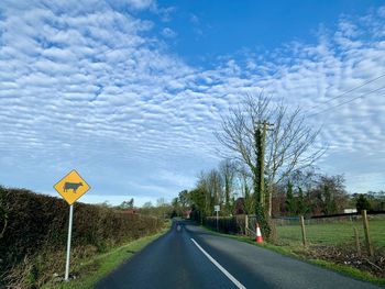 Road sign by trees against sky