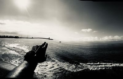 Person holding umbrella by sea against sky