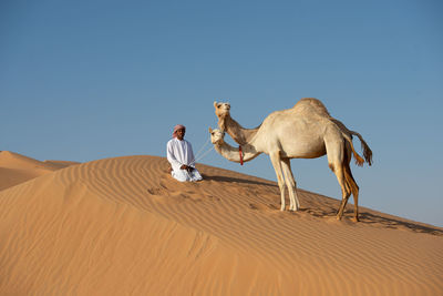 Man on sand dune in desert against clear sky