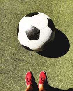 Low section of person wearing red shoes by big soccer ball on field