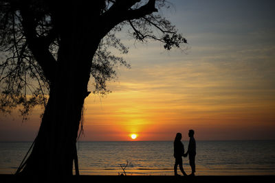 Silhouette people on beach against sky during sunset