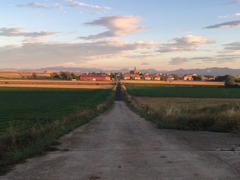 Road amidst field against sky during sunset