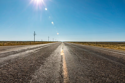 Surface level of country road against clear blue sky