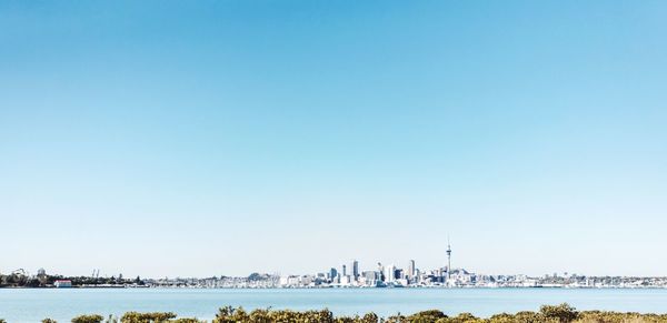 Distant view of cityscape with sea against clear sky