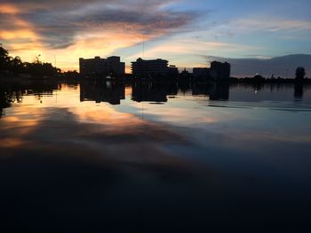 Silhouette buildings by lake against sky during sunset