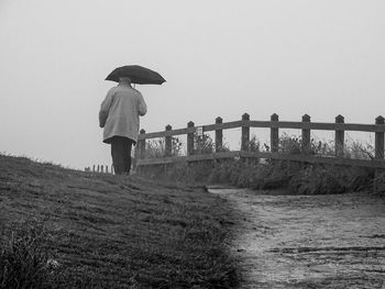 Man with umbrella walking on field against clear sky