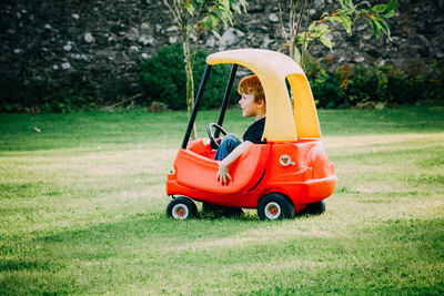 Boy sitting in toy car on grassy field