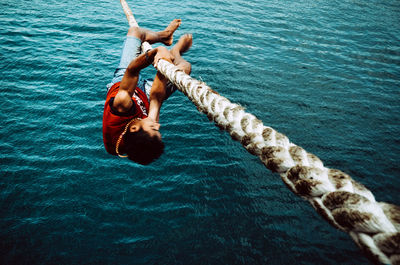 Full length of young man hanging on rope over sea